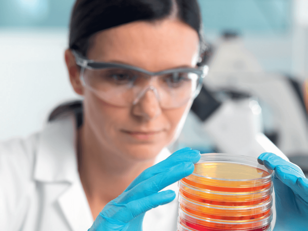 Bild på  en person i labbkläder och handskar som håller i ett labbprov